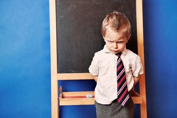 a child standing in front of a chalk board with his head down and his arms behind his back